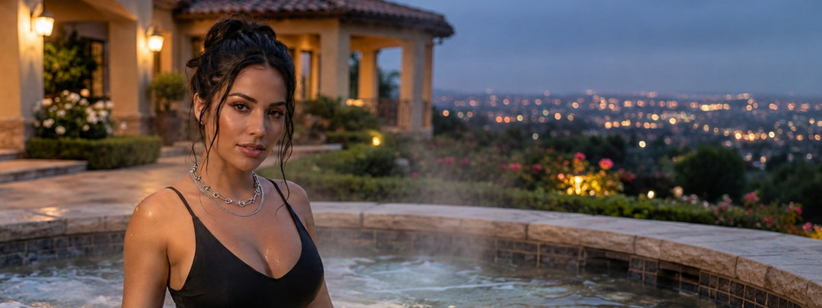A woman in a black swimsuit standing in a hot tub with a city skyline and a villa in the background at dusk.